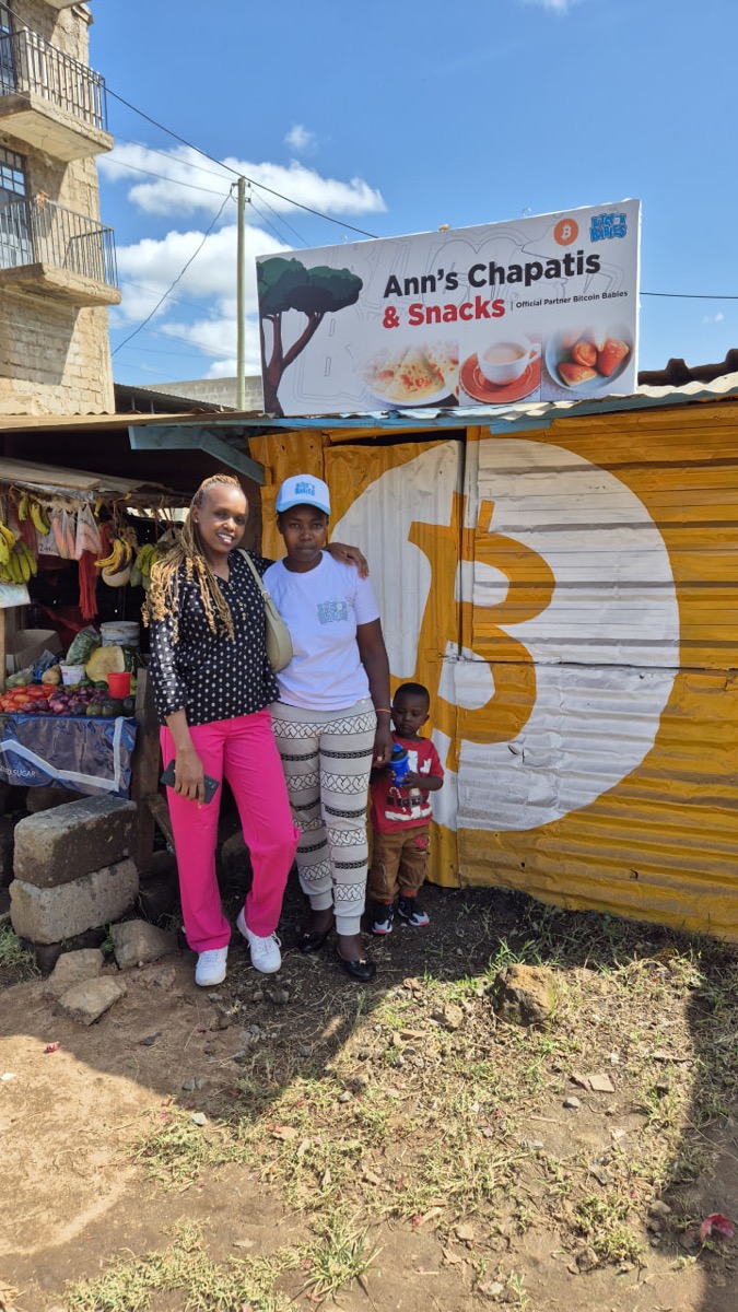 Local women and child in front of Ann's Chapatis & Snacks, painted with a Bitcoin logo